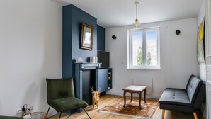 En stue med en mørkeblå accentvæg, pejs, fjernsyn, et vindue med udsigt og en grøn lænestol.