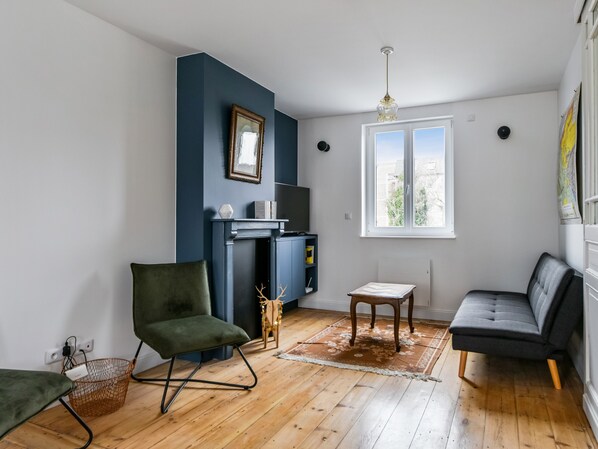 A living room with a dark blue accent wall, a fireplace, a television, a window with a view, and a green chair.