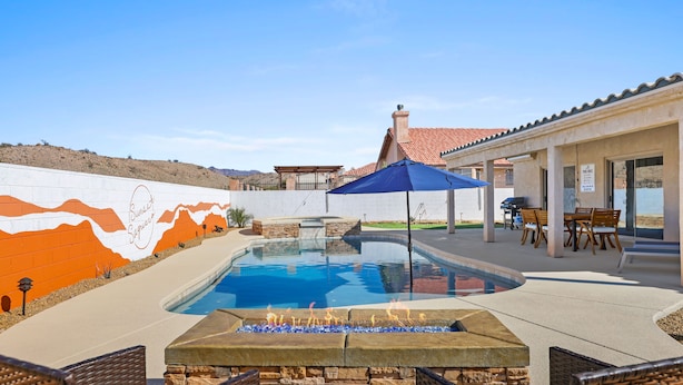 Una piscina con una chimenea, asientos al aire libre y un mural en la pared.