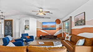 Una sala de estar moderna con un televisor grande, sofás de cuero y un ventilador de techo.