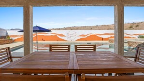 Un restaurante con una mesa y sillas de madera, un paraguas azul y un mural de montañas al fondo.