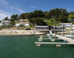 A coastal area with a pier, a small wooden structure, and houses in the background. - Lowenna Manor 5 (Wadebridge)