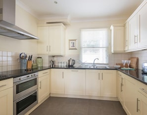 A kitchen with light-colored cabinets, a double oven, a sink, and a window with blinds. - Lowenna Manor 5 (Wadebridge)
