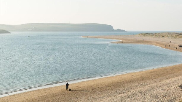 Une plage où une personne se promène le long du rivage, une plage de sable et une mer calme.