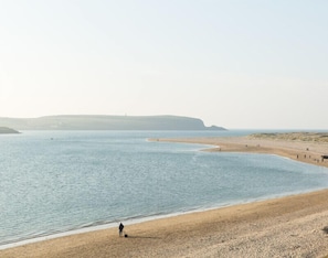 A beach with a person walking along the shore, a sandy beach, and a calm sea. - Lowenna Manor 5 (Wadebridge)