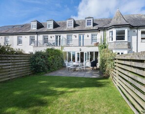 A two-story building with a patio area, a covered seating area, and a fenced garden. - Lowenna Manor 5 (Wadebridge)