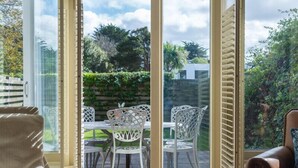 Une pièce dotée d’une porte-fenêtre coulissante donnant sur un patio extérieur aménagé avec des meubles en osier blanc et une table.