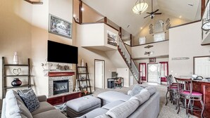 A spacious living room with a large gray sectional sofa, a fireplace, and a staircase leading to an upper level. - Waterfront Lake Eufaula Home: Multi-Level Balcony (Eufaula)