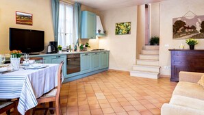 Een compacte keuken met blauwe kastjes, een eettafel gedekt met borden en glazen, en een televisie aan de linkerkant.