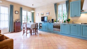 Een ruime keuken met blauwe kastjes, een eettafel met stoelen en een televisie.