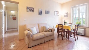 A living room with a beige sofa, dining table with chairs, and a window with curtains. - Apartment in a historic Villa _"IL PALIO"_view & authentic hospitality in Siena (Siena)