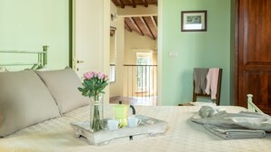 Un dormitorio con cama, una bandeja con tazas y una tetera, un florero con flores y una puerta de madera.