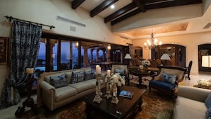 A spacious living room with a high ceiling, large windows, and a view of the outdoors.