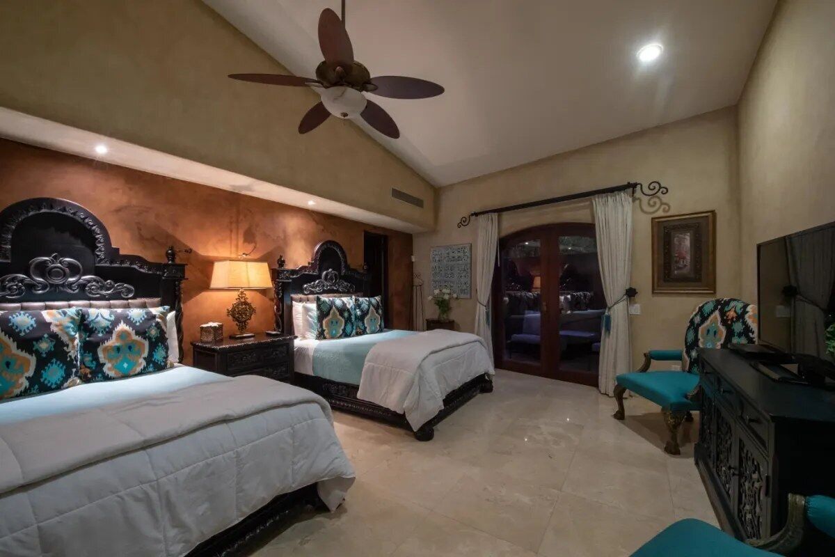 A hotel room with two beds, a ceiling fan, a TV, and a view of the outside.
