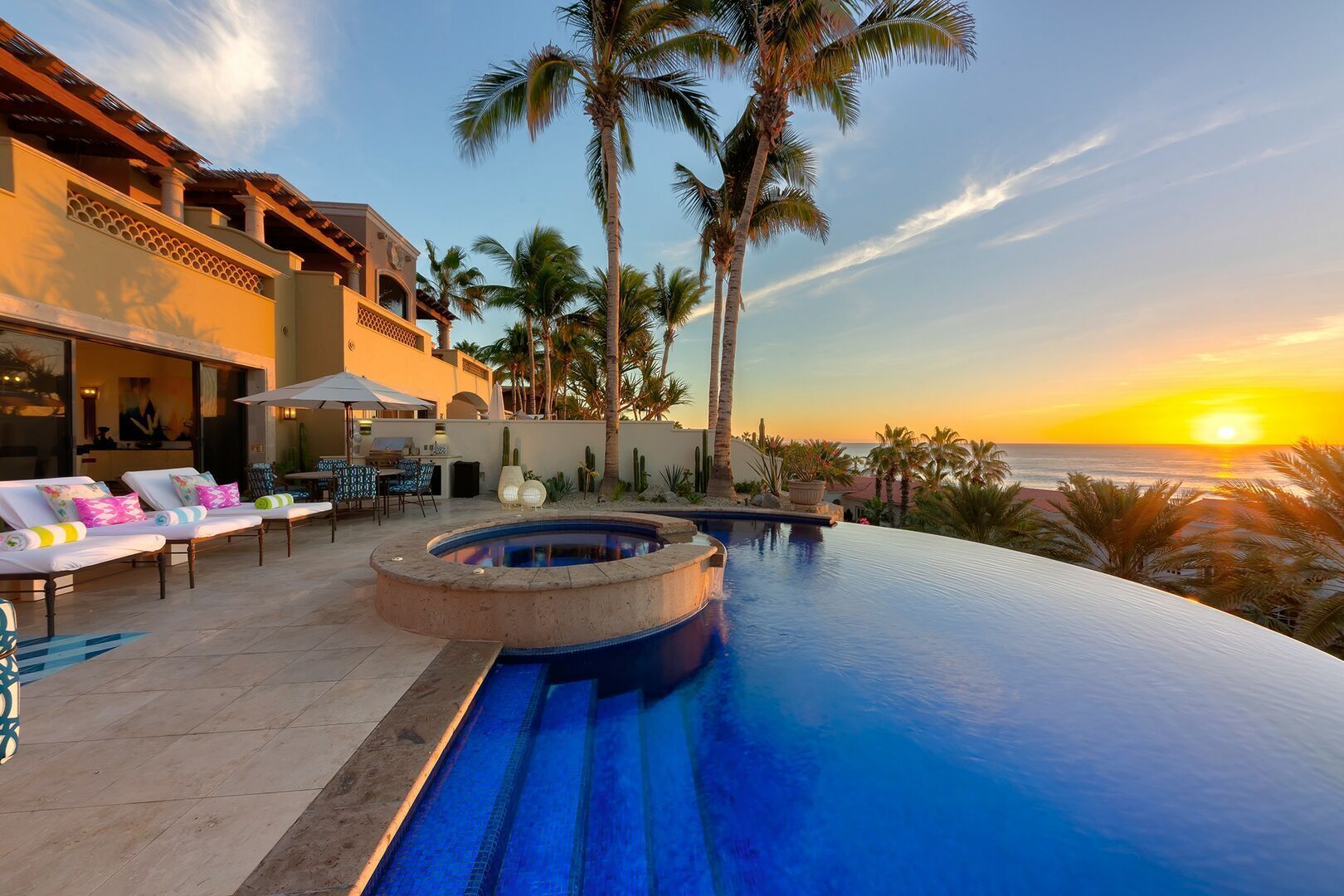 An infinity pool with a hot tub, lounge chairs, and palm trees.