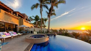 Una piscina infinita con un jacuzzi, sillones de descanso y palmeras.