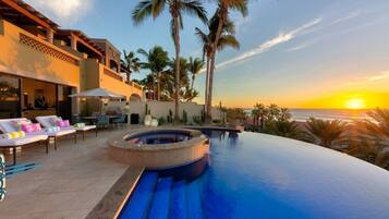 An infinity pool with a hot tub, lounge chairs, and palm trees.