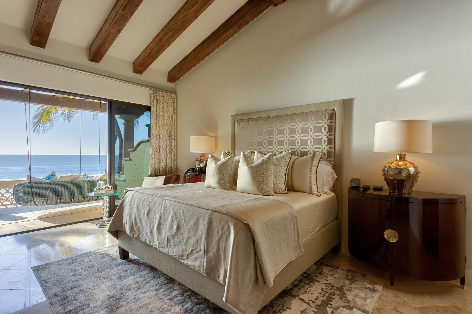 A bedroom with a large bed, a nightstand, a lamp, and a view of the ocean.