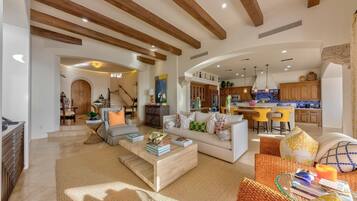 A spacious living area with a high ceiling, wooden beams, and a kitchen in the background.