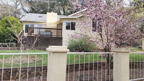 A residential property with a fenced yard, a small house with a balcony, and blooming trees.