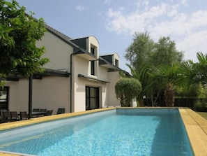 Una casa moderna con piscina, rodeada de vegetación y un cielo despejado.