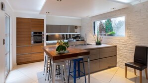 Een moderne keuken met een centraal eiland, barkrukken, een eettafel en een raam met uitzicht op bomen.