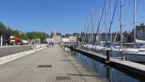 Een jachthaven met boten afgemeerd langs het water, een verharde promenade en gebouwen op de achtergrond.