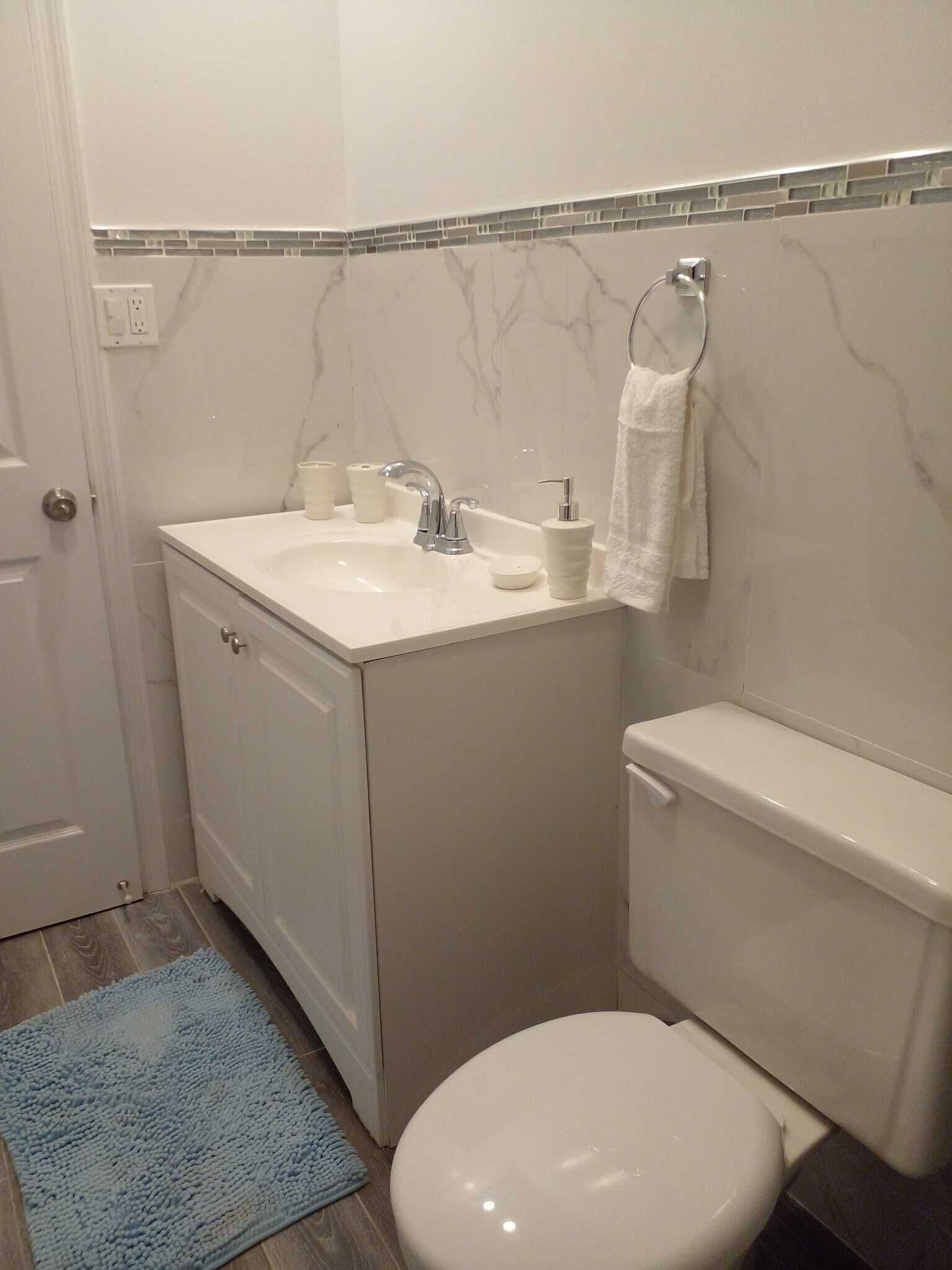 Une salle de bain avec un lavabo blanc, des toilettes et un tapis bleu.