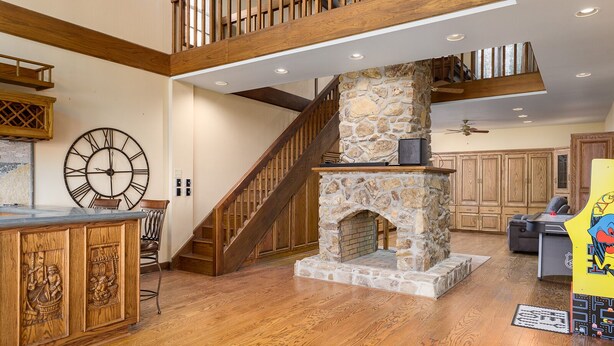 A spacious living area with a stone fireplace, wooden staircase, and a large clock on the wall.