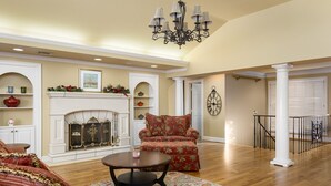 A spacious living room with a fireplace, a red armchair, a coffee table, and a chandelier.