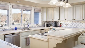 A spacious kitchen with a large island, white cabinetry, and a view of the outdoors through the windows.