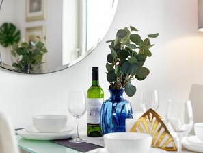 Uma mesa de jantar com uma garrafa de vinho, um copo e um vaso com folhas verdes.