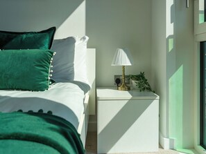 Une chambre à coucher avec un lit, des oreillers, une table de chevet avec une lampe et une plante.