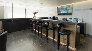 A modern kitchen with a bar area, featuring a large TV, bar stools, and a vase with flowers.