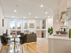 A modern apartment with a dining area, kitchen, and large windows offering city views.