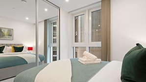 A modern hotel room with a large bed, a mirror, a window with a view of a building, and a red lamp on the nightstand. - Cosy apartment for 2 guests with WIFI and TV (London)