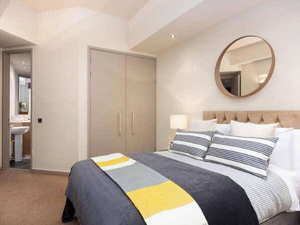 A hotel room with a bed, a round mirror, a wardrobe, and a bathroom visible through an open door.