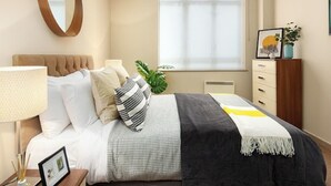 A modern bedroom with a bed, bedside table, lamp, and a large window with blinds. - Lovely apartment for 2 people with WIFI and TV (London)