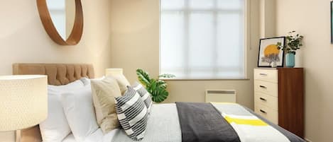 A modern bedroom with a bed, bedside table, lamp, and a large window with blinds.