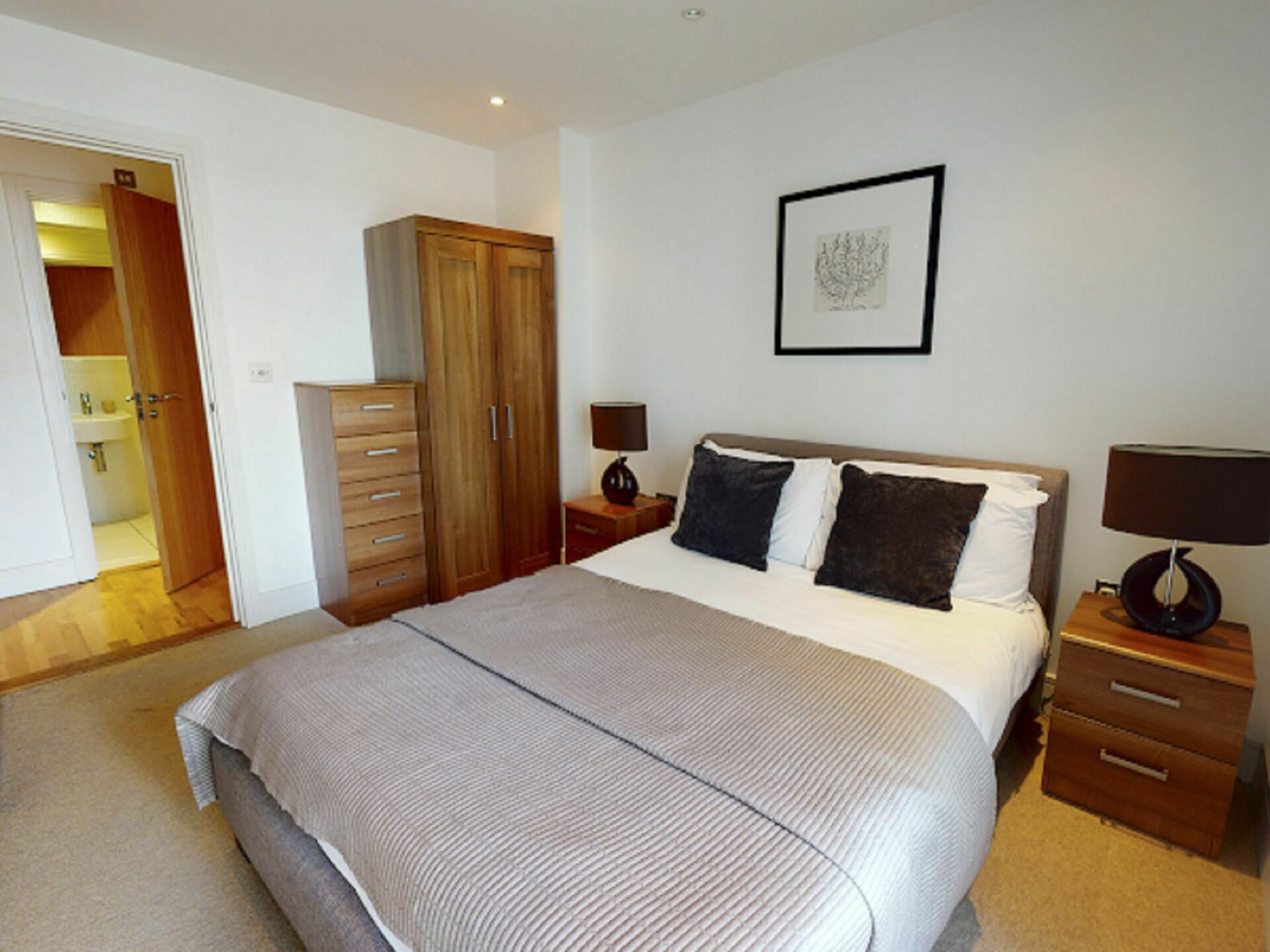 A bedroom with a large bed, wooden wardrobe, bedside tables, and a framed picture on the wall.