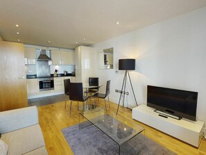 A modern living room with a flat-screen TV, a glass coffee table, and a dining area with chairs.
