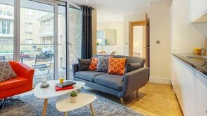 A modern living room with a sofa, a red chair, a small coffee table, and a kitchen area with a counter and cabinets. - Nice apartment for 4 guests with WIFI, TV and balcony (London)