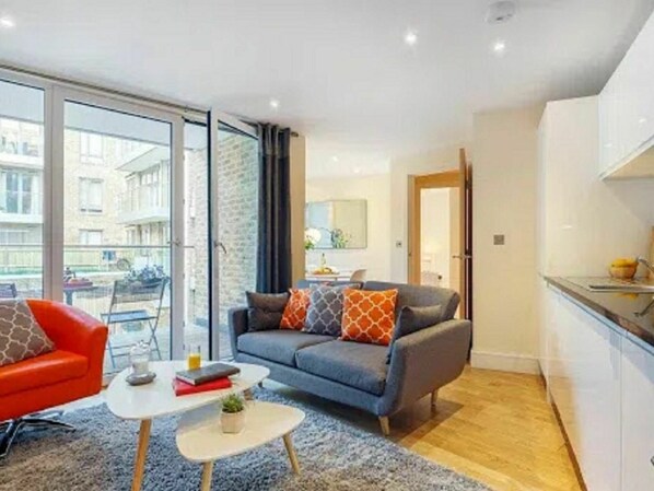 A modern living room with a sofa, a red chair, a small coffee table, and a kitchen area with a counter and cabinets.