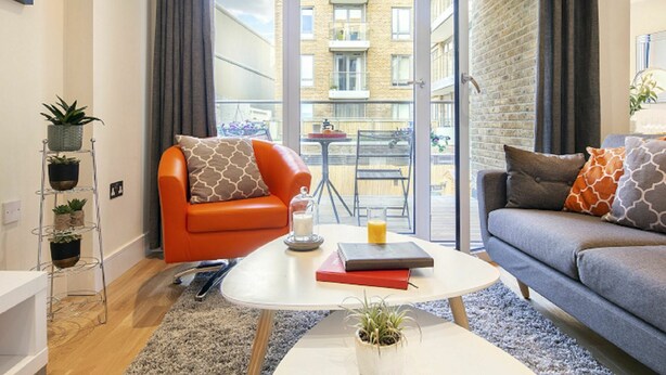 A modern apartment with a sofa, armchair, and a small table with books and a candle. - Nice apartment for 4 guests with WIFI, TV and balcony (London)