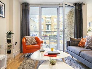 A modern apartment with a sofa, armchair, and a small table with books and a candle.