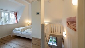 A bedroom with a sloped ceiling, a bed, a window with curtains, and a painting on the wall. - Vacation apartment Oldsum - Take a vacation in the artists' village of Oldsum (Oldsum)