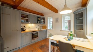 A kitchen with grey cabinets, a wooden ceiling, a tiled floor, a sink, a stove, and a dining table with chairs. - Vacation apartment Oldsum - Take a vacation in the artists' village of Oldsum (Oldsum)
