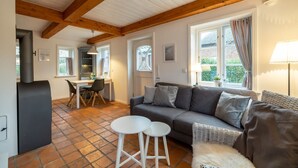 A cozy living room with a grey sofa, a small white table, and a dining area with a table and chairs. - Vacation apartment Oldsum - Take a vacation in the artists' village of Oldsum (Oldsum)