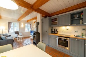 Un salon chaleureux avec une cheminée, un coin repas et une cuisine dotée de meubles gris et d’un dosseret carrelé.