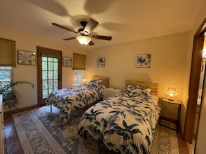 Une chambre avec deux lits, un ventilateur de plafond et une fenêtre donnant sur un paysage verdoyant.